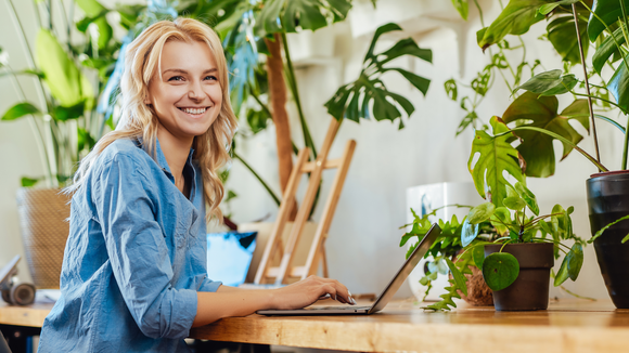 Professional female business person does her work on a laptop in modern and cosy office. Eco and warm office room with plants.